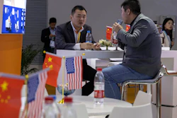 In this Nov. 6, 2019, file photo, visitors chat near American and Chinese flags displayed at a booth for an American company promoting environmental sensors during the China International Import Expo in Shanghai.