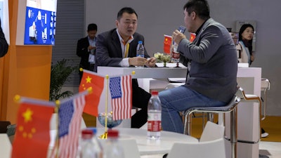 In this Nov. 6, 2019, file photo, visitors chat near American and Chinese flags displayed at a booth for an American company promoting environmental sensors during the China International Import Expo in Shanghai.