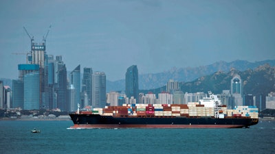 In this Sept. 13, 2018, file photo, a container ship sails by the business district in Qingdao, China.