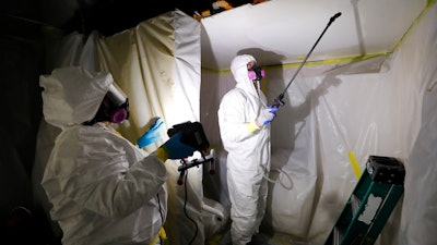 In this Oct. 18, 2017, file photo, Asbestos Removal Technologies Inc. job superintendent Ryan Laitila, right, sprays amended water as job foreman Megan Eberhart holds a light during asbestos abatement in Howell, Mich.