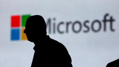In this Nov. 7, 2017, file photo, an unidentified man is silhouetted as he walks in front of Microsoft logo at an event in New Delhi, India.