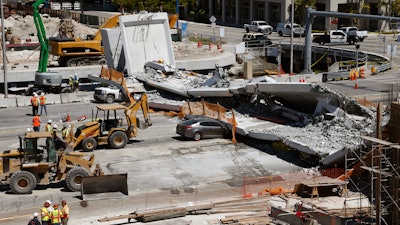 In this March 16, 2018, file photo, crushed cars lie under a section of a collapsed pedestrian bridge near Florida International University in Miami. Federal transportation officials have concluded that design flaws and a lack of oversight led to the collapse of the pedestrian bridge that killed six people last year.