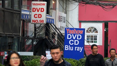 In this April 27, 2016, file photo, people walk past a shop selling pirated movie DVDs and music CDs in Beijing. China’s leaders have issued new, tougher guidelines for protection of patents, copyrights and other intellectual property.