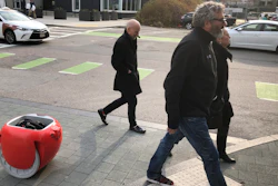 Piaggio Fast Forward CEO Greg Lynn, center, is followed by his company's Gita carrier robot as he crosses a street on Monday, Nov. 11, in Boston. The two-wheeled machine is carrying a backpack and uses cameras and sensors to track its owner.