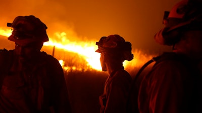 In this Sept. 12, 2015 file photo, California Department of Corrections and Rehabilitation inmates stand guard as flames from the Butte Fire approach a containment line near San Andreas, Calif. California Gov. Gavin Newsom is stepping up pressure on Pacific Gas and Electric to fork over billions more in cash to pay thousands of people whose homes burned in wildfires that drove the utility into bankruptcy. The rising tensions were expected to surface at a hearing Wednesday, Nov. 13, 2019, that has been abruptly postponed by a week.
