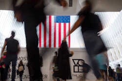 In this Sept. 11, 2019, photo people walk past an American flag at the start of a work day at the Oculus, part of the World Trade Center transportation hub, in New York.