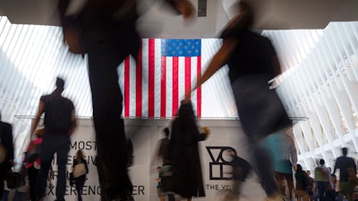 In this Sept. 11, 2019, photo people walk past an American flag at the start of a work day at the Oculus, part of the World Trade Center transportation hub, in New York.