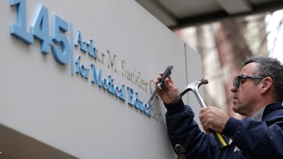 Worker Gabe Ryan removes a sign that includes the name Arthur M. Sackler at an entrance to Tufts School of Medicine, Dec. 5, 2019, in Boston.