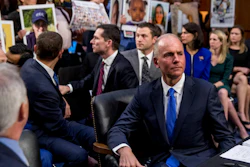 In this Oct. 29, 2019, file photo, Boeing President and CEO Dennis Muilenburg, right foreground, watches as family members hold up photographs of those killed in the Ethiopian Airlines Flight 302 and Lion Air Flight 610 crashes during a Senate committee hearing on Capitol Hill.