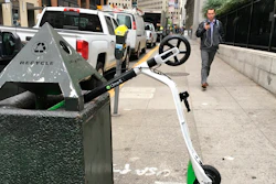 In this photo taken May 14, 2018, a man walks past an electric scooter that dumped into a trash can in San Francisco.