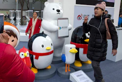 In this Nov. 20, 2017, file photo, a woman walks past mascots representing platforms owned by Tencent Holdings Limited in Beijing.