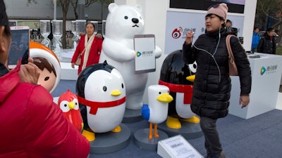 In this Nov. 20, 2017, file photo, a woman walks past mascots representing platforms owned by Tencent Holdings Limited in Beijing.