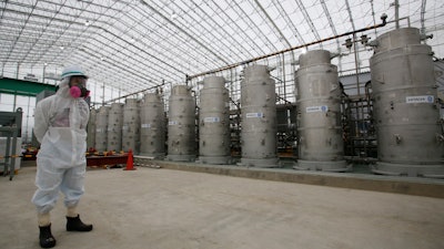 In this Nov. 12, 2014, file photo, a Tokyo Electric Power Co. official wearing a radioactive protective gear stands in front of Advanced Liquid Processing Systems during a press tour at the Fukushima Dai-ichi nuclear power plant in Okuma