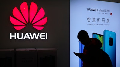 In this Dec. 11, 2018, photo, a man browses his smartphone outside a Huawei store at a shopping mall in Beijing.