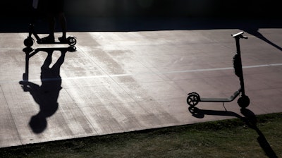 In this May 28, 2019, file photo, a man on a scooter passes a parked scooter along the Mission Beach boardwalk in San Diego.