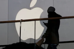In this Dec. 23, 2013, file photo, a woman using a phone walks past Apple's logo near its retail outlet in Beijing.