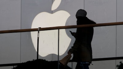 In this Dec. 23, 2013, file photo, a woman using a phone walks past Apple's logo near its retail outlet in Beijing.