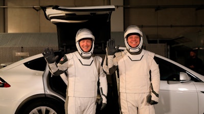 In this Jan. 17, 2020, photo, astronauts Doug Hurley, left, and Robert Behnken pose in front of a Tesla Model X at a SpaceX launch dress rehearsal at Kennedy Space Center in Florida.