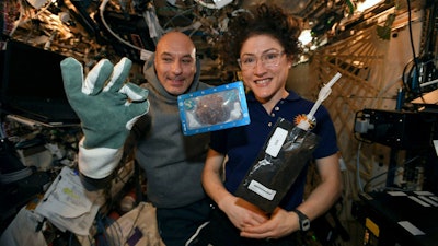 In this photo made available by U.S. astronaut Christina Koch via Twitter on Dec. 26, 2019, she and Italian astronaut Luca Parmitano pose for a photo with a cookie baked on the International Space Station.