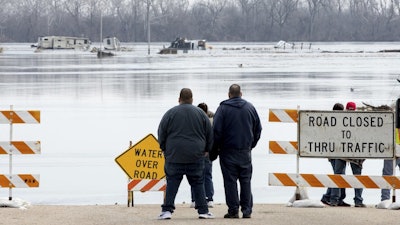 People stand at the edge of a flooded road in Plattsmouth, Neb., March 17, 2019.