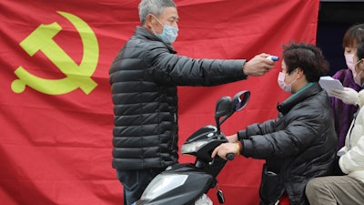 A volunteer takes the temperature of a scooter driver at a roadside checkpoint in Hangzhou, China, Feb. 3, 2020.