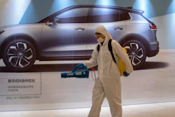 A worker disinfects a mall near an advertisement for a car in Beijing, Feb. 12, 2020.