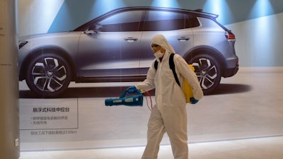 A worker disinfects a mall near an advertisement for a car in Beijing, Feb. 12, 2020.