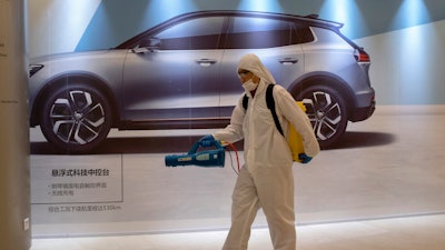 A worker disinfects a mall near an advertisement for a car in Beijing, Feb. 12, 2020.