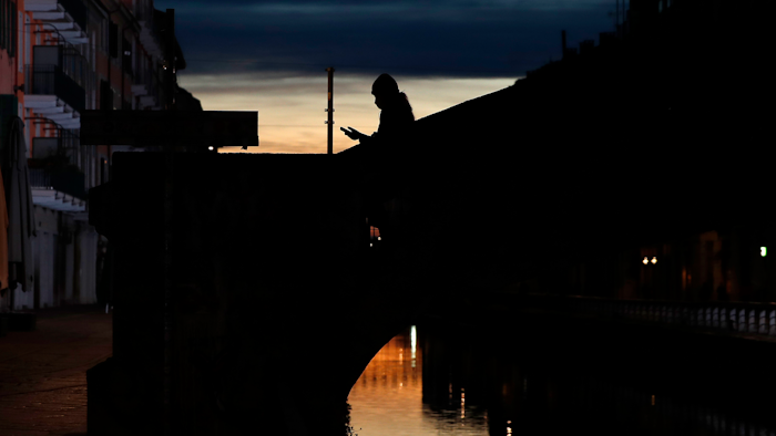 A woman wearing a face mask checks her phone as she walks at the Naviglio Grande canal in Milan, March 10, 2020.