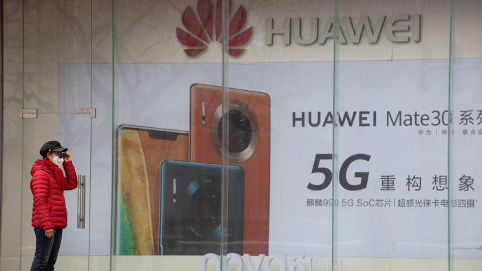 A woman stands near an advertisement for Huawei mobile phones in Beijing, March 8, 2020.