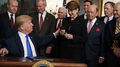 President Donald Trump hands a pen to Lockheed Martin CEO Marillyn Hewson after signing a memorandum imposing tariffs and investment restrictions on China, March 22, 2018, in the White House.
