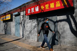 A man wearing a protective face mask walks by shuttered business shops in Beijing, March 1, 2020.