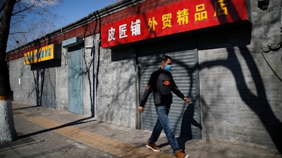 A man wearing a protective face mask walks by shuttered business shops in Beijing, March 1, 2020.