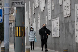 Residents walk outside a closed school in Beijing, Feb. 25, 2020.