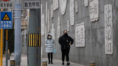 Residents walk outside a closed school in Beijing, Feb. 25, 2020.