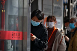 People wait to get temperature checks before entering a bank in Beijing, March 11, 2020.