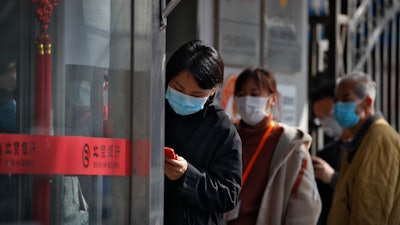 People wait to get temperature checks before entering a bank in Beijing, March 11, 2020.
