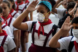 Students, some wearing protective masks, recite the national anthem in Havana, March 13, 2020.