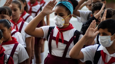 Students, some wearing protective masks, recite the national anthem in Havana, March 13, 2020.
