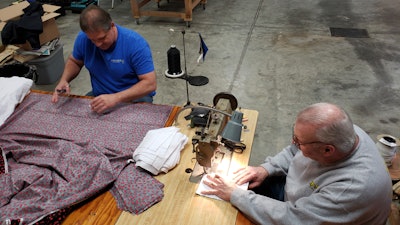 Bill Purdue, left, cuts pieces of fabric while Mike Rice sews them into face masks in Rice's auto body and upholstery shop in Washington, Ind., March 22, 2020.