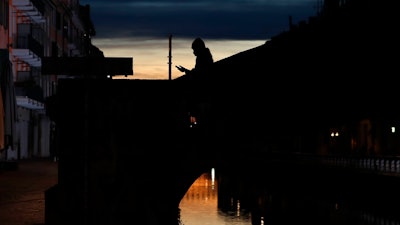 A woman wearing a face mask checks her phone as she walks at the Naviglio Grande canal in Milan, March 10, 2020.
