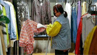 A worker wearing a protective face mask irons clothes at a re-opened shopping mall in in Wuhan, March 30, 2020.