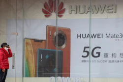 A woman stands near an advertisement for Huawei mobile phones in Beijing, March 8, 2020.