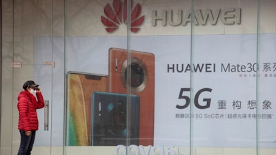 A woman stands near an advertisement for Huawei mobile phones in Beijing, March 8, 2020.