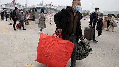 Residents carry their belongings as they walk past a toll booth to enter the city of Wuhan, April 2, 2020.