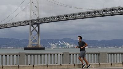 A man wears a mask while running in front of the San Francisco-Oakland Bay Bridge, April 5, 2020.