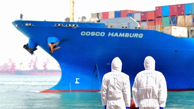 Workers in protective suits near a COSCO container ship docked at a port in Qingdao, China, March 31, 2020.