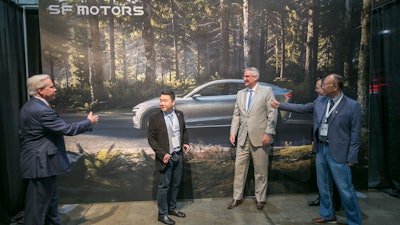 SF Motors CEO John Zhang, second from left, and Indiana Gov. Eric Holcomb, second from right, pose for picture in front of a mural of the SF 7, the company's electric vehicle, on Wednesday, May 30, 2018, in Mishawaka, Ind. SF Motors, an electric vehicle startup, announced Wednesday that it is retooling an Indiana factory and hopes to conduct trial runs for two new lines of vehicles by the end of the year.