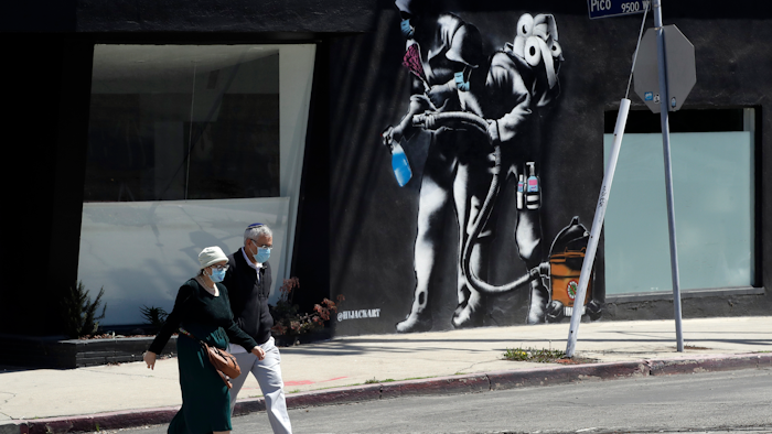 People wearing masks walk past a mural depicting a coronavirus theme in Los Angeles, April 14, 2020.
