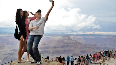 Tourists Joseph Lin, Ning Chao, center, and Linda Wang, left, pose along the south rim at Grand Canyon National Park, Ariz., Aug. 2, 2015.